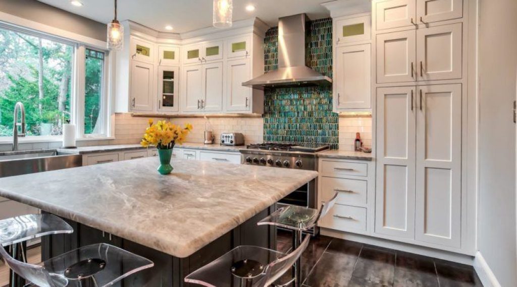 Kitchen designed by Main Line Kitchen Design in Swarthmore, PA featuring white Brighton inset cabinetry in the Cascade door style with distinctive grey marble countertops and a kitchen island with open shelving on one side and countertop seating on two sides.