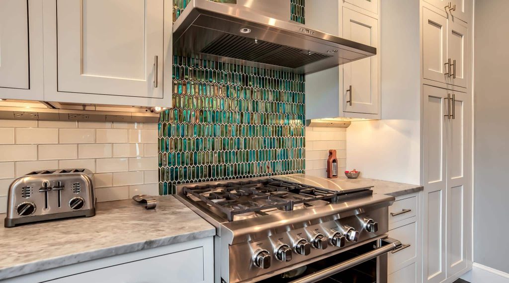 Kitchen featuring an aqua and jade mosaic backsplash behind a stainless steel gas range with griddle.